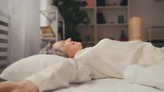 Side view of a happy senior woman falling on a comfortable bed in slow motion