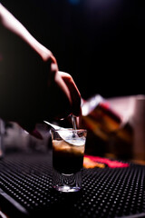 Bartender pours triple sec into a shot using a bartender's spoon. Preparing shot b52. Mixing an...