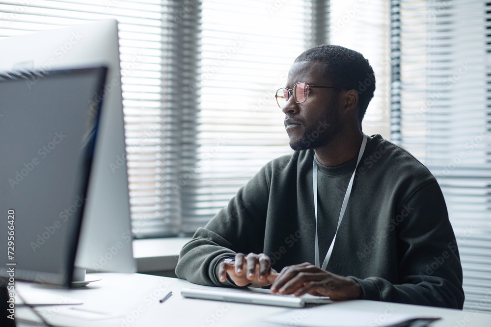 Fototapete graphic minimal portrait of young black man looking at computer screen while working in it office ag