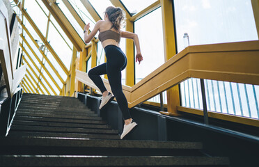 Dynamic young Caucasian woman sprinting up the stairs in an architecturally striking yellow...