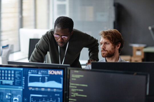 Portrait of two male professionals discussing work issues over computer monitors in cybersecurity office copy space