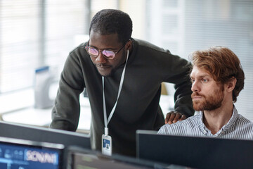 Portrait of young Black man mentoring bearded IT developer and reviewing code looking at computer...