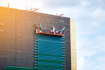 Worker on aerial platform, cladding wall with corrugated sheets. Worker on construction cradle...