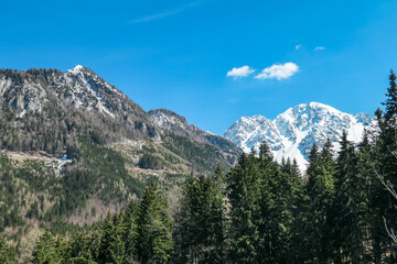 Scenic view of snow capped mountain peak Hochstuhl (Stol) seen from Bärental in Karwanks, Carinthia, Austria. Remote alpine landscape in springtime in Austrian Alps, Europe. Idyllic trail in forest
