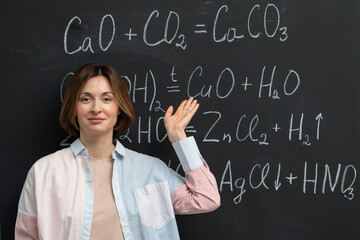 Back view of a female student writing the formula of a chemical reaction on the blackboard