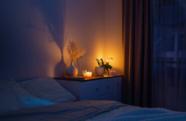burning candles with flowers in vase in bedroom at night