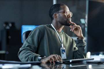 Side view portrait of Black young man wearing glasses and thinking in pro company office looking...