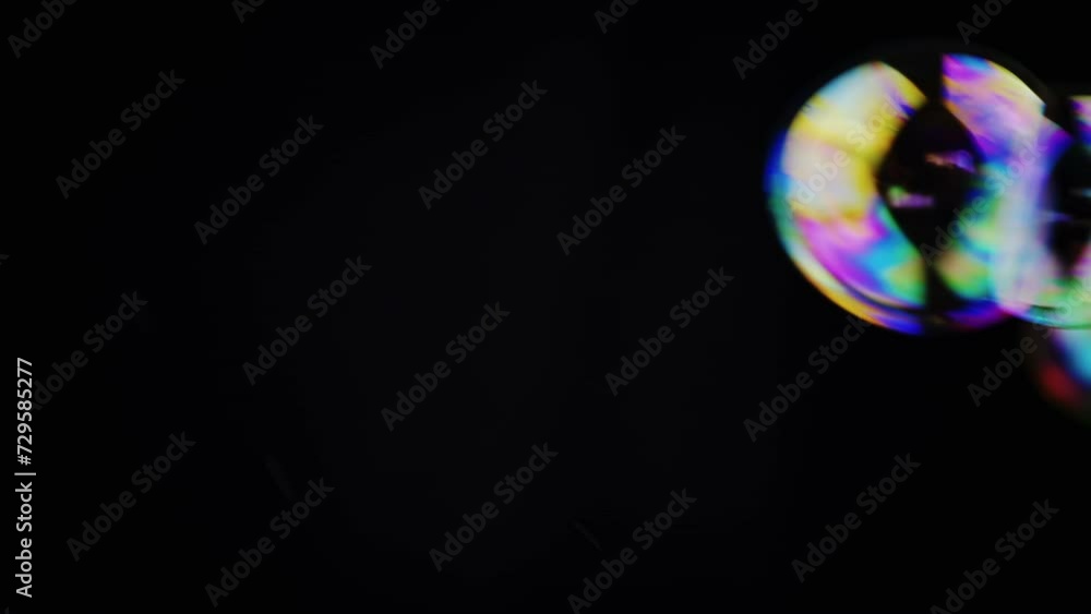 Poster colorful soap bubbles fly in an empty space on isolated black background. many rainbow transparent b