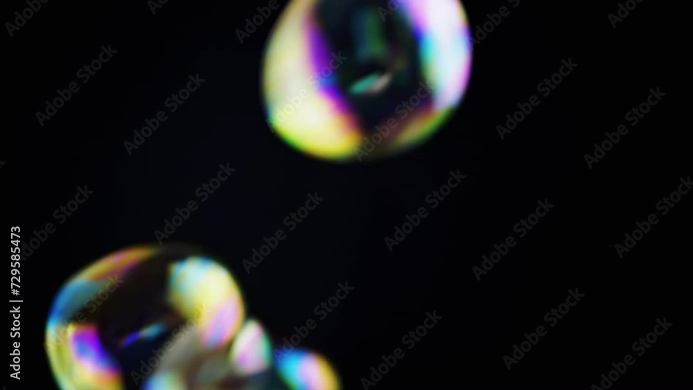 Poster colorful soap bubbles fly in an empty space on isolated black background. many rainbow transparent b
