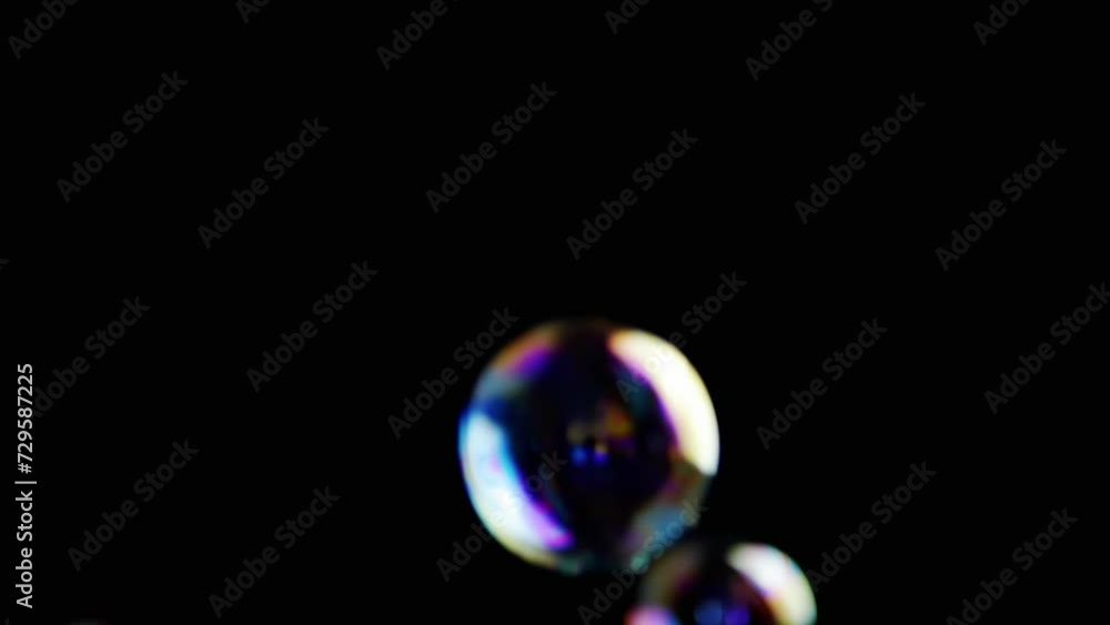 Poster colorful soap bubbles fly in an empty space on isolated black background. many rainbow transparent b