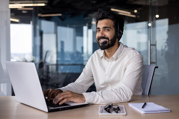 Smiling indian businessman in office setting with laptop and headset, professional at work