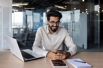 Indian businessman working in office environment on laptop and smartphone