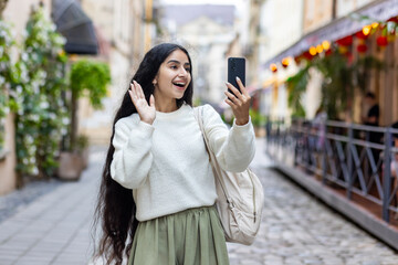 Joyful indian woman using smartphone for video call on city street