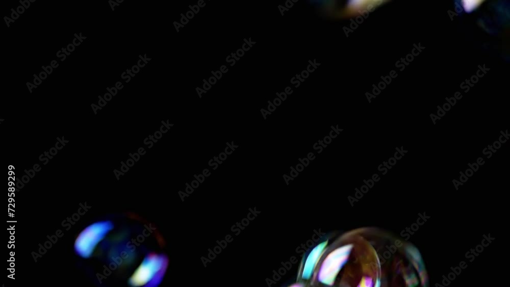 Poster colorful soap bubbles fly in an empty space on isolated black background. many rainbow transparent b