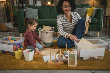 Mother and toddler daughter at home collect toys put in box clean room