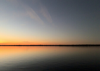 Distant shore highlighted by vibrant sunset colors reflected in still water