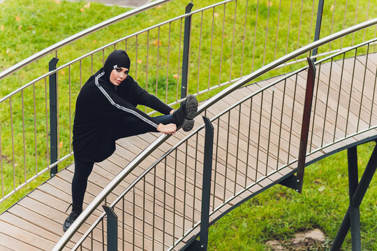 Hijab girl exercising on walkway bridge in early morning. Muslim woman wearing sports clothes doing stretching workout outdoors. - Powered by Adobe