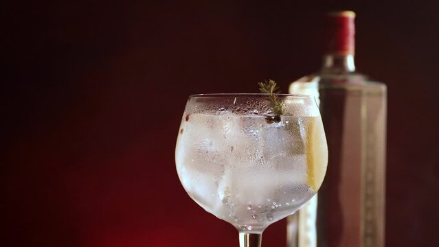 Gin tonic cup with ice rotating on dark red smoking background. Horizontal video.