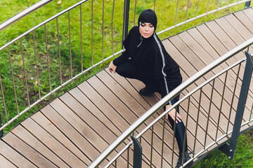 Hijab girl exercising on walkway bridge in early morning. Muslim woman wearing sports clothes doing stretching workout outdoors.