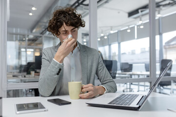 Professional male with curly hair sipping coffee while focusing on laptop work in a bright...