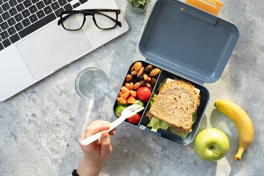 Healthy business lunch at workplace. Sandwich, vegetables, fruid and water lunch box on working desk with laptop, glasses.