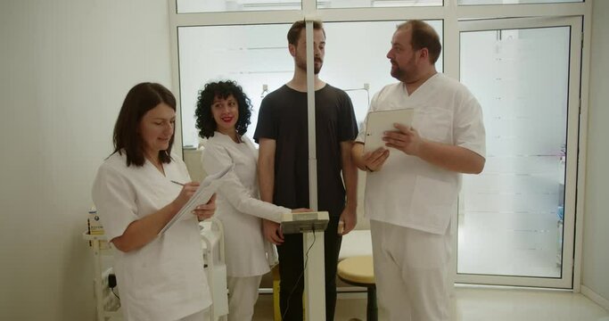 Young patient discussing with doctor while he and two nurses are measuring his height using stadiometer.
