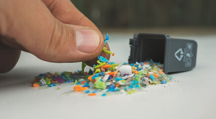 Macro shot of fingers taking particles of micro plastics from a mini plastic trash can. Concept of...