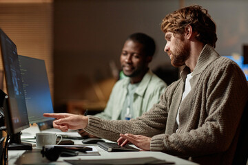 Side view portrait of bearded man pointing at computer screen and talking to colleague while...