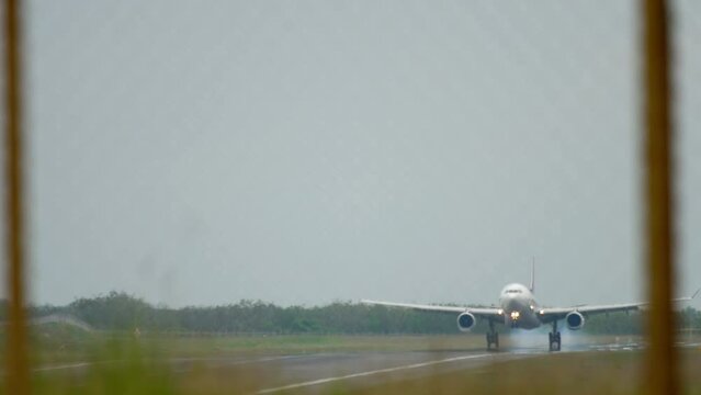 View through the fence of a passenger plane with an unrecognizable livery landing, touching the runway and braking