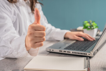 Woman giving thumbs up while working in office, business concept