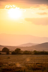 Stunning sunset over the countryside of Bulgaria. Mountain hills in the distance. Beautiful yellow orange skies and trees in the distance.