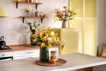 A bouquet of flowers on a wooden table. In the background, the interior of a white kitchen in the Scandinavian style. The concept of home comfort.