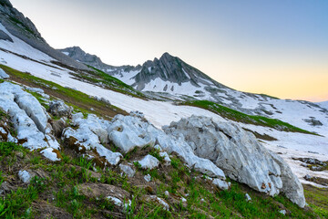 The snowdrifts and green grass on top of mountains in the tropical forest at sunrise. The alpine mountains and meadows.