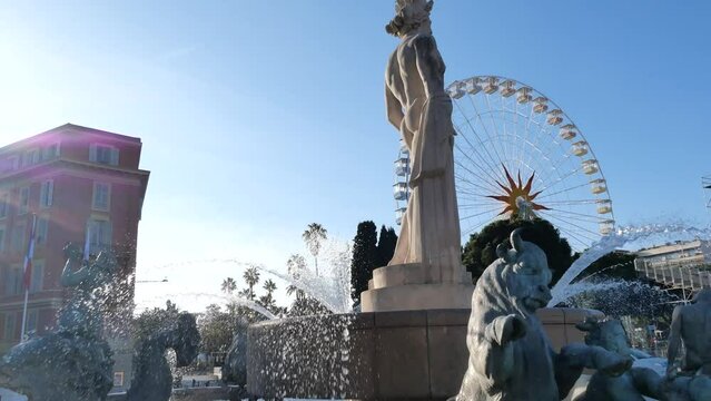 Dynamic scenes at Place Mass&eacute;na near the Fontaine du Soleil, with the iconic bronze sculpture of the Greek god Apollo, alongside the famous Ferris wheel, capturing the essence of winter 2024 in Nice