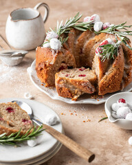 Christmas bundt cake decorated with glaze, cranberries and rosemary served on beige table. Homemade cake recipe