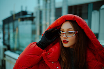 Fashionable confident woman wearing trendy oversized red puffer down jacket with hood, y2k glasses,...