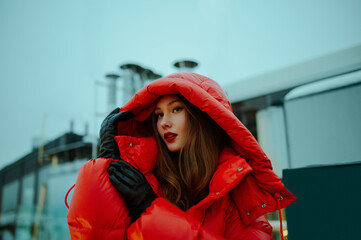 Fashionable confident woman wearing trendy oversized red puffer down jacket with hood, black...