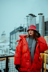 Fashionable confident woman wearing trendy oversized red puffer down jacket with hood, quilted leather bucket hat, posing outdoor. Street style fashion portrait. Copy, empty space for text