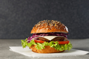 Vegan burger with vegetables and sauce on paper on dark background. Healthy food concept.