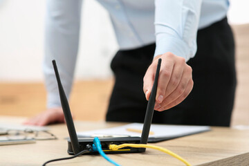 Man adjusting antenna of Wi-Fi router at wooden table indoors, closeup