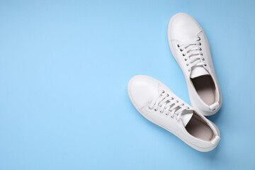 Pair of stylish white sneakers on light blue background, top view. Space for text