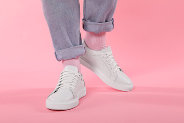 Woman wearing stylish white sneakers on pink background, closeup
