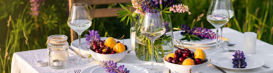 Sunset, golden hour. Romantic table decor for loving couple on blooming meadow with purple lupines....