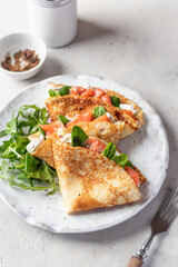 Crepes or thin pancakes with smoked salmon, soft cheese and spinach on a plate on gray textured background. Pancake day, Maslenitsa