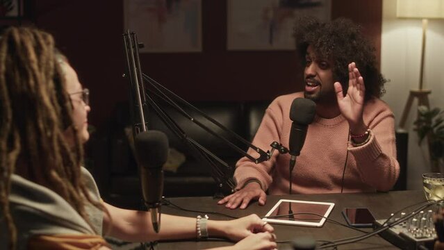 Waist up of ethnically diverse young man and woman having emotional discussion while recording podcast together at night studio - Powered by Adobe