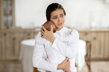 Exhausted young mother holding little baby girl, standing at home interior, tired european mom,...