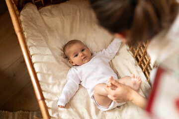 Mother dresses cute little baby girl, playing with baby while kid lying on bed. Happy motherhood, infant baby, mother's day