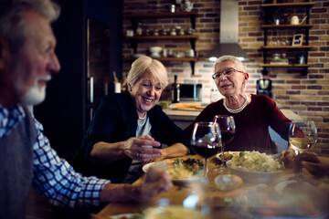 Happy senior people eating dinner together at home - obrazy, fototapety, plakaty
