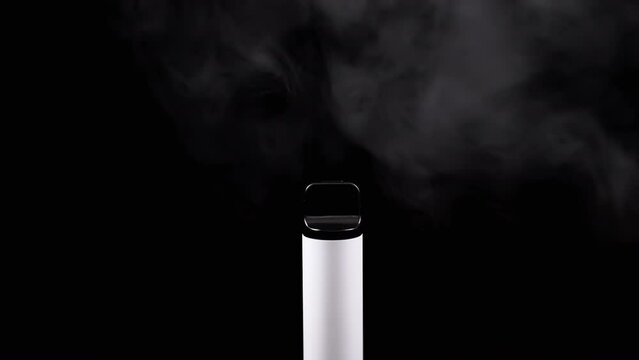 White Electronic Cigarette or Vape in Smoke on a Black Background in Empty Space. E-cigarette. Blurred motion. Steam texture. Thick puffs of gray smoke. Bad habits. Alternative. Smoking. Slow motion.