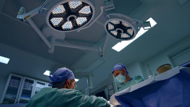 Round lamps on the ceiling of operational room. Two medics work near the surgical table. Low angle view.
